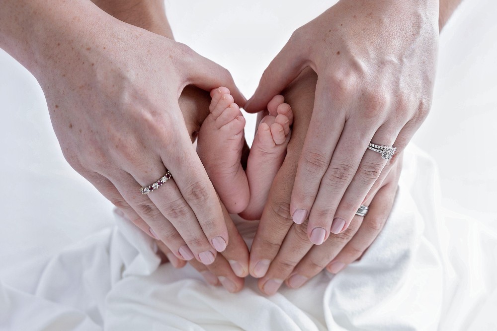 Newborn baby toes nestled in parents’ hands forming a heart, Essex family photography moment